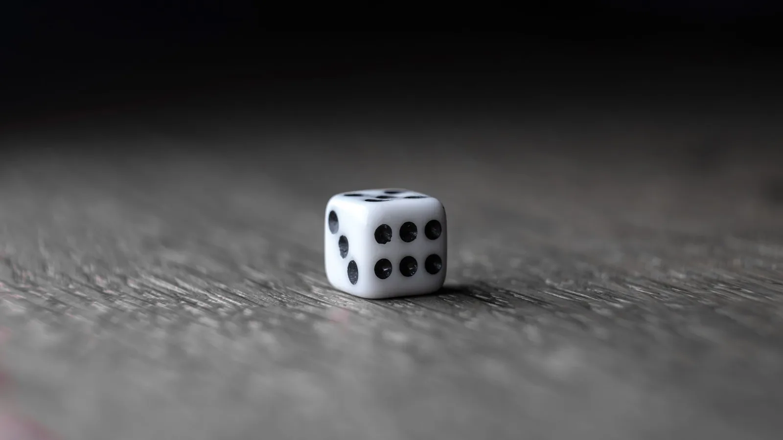 A single white die lying on a wooden table